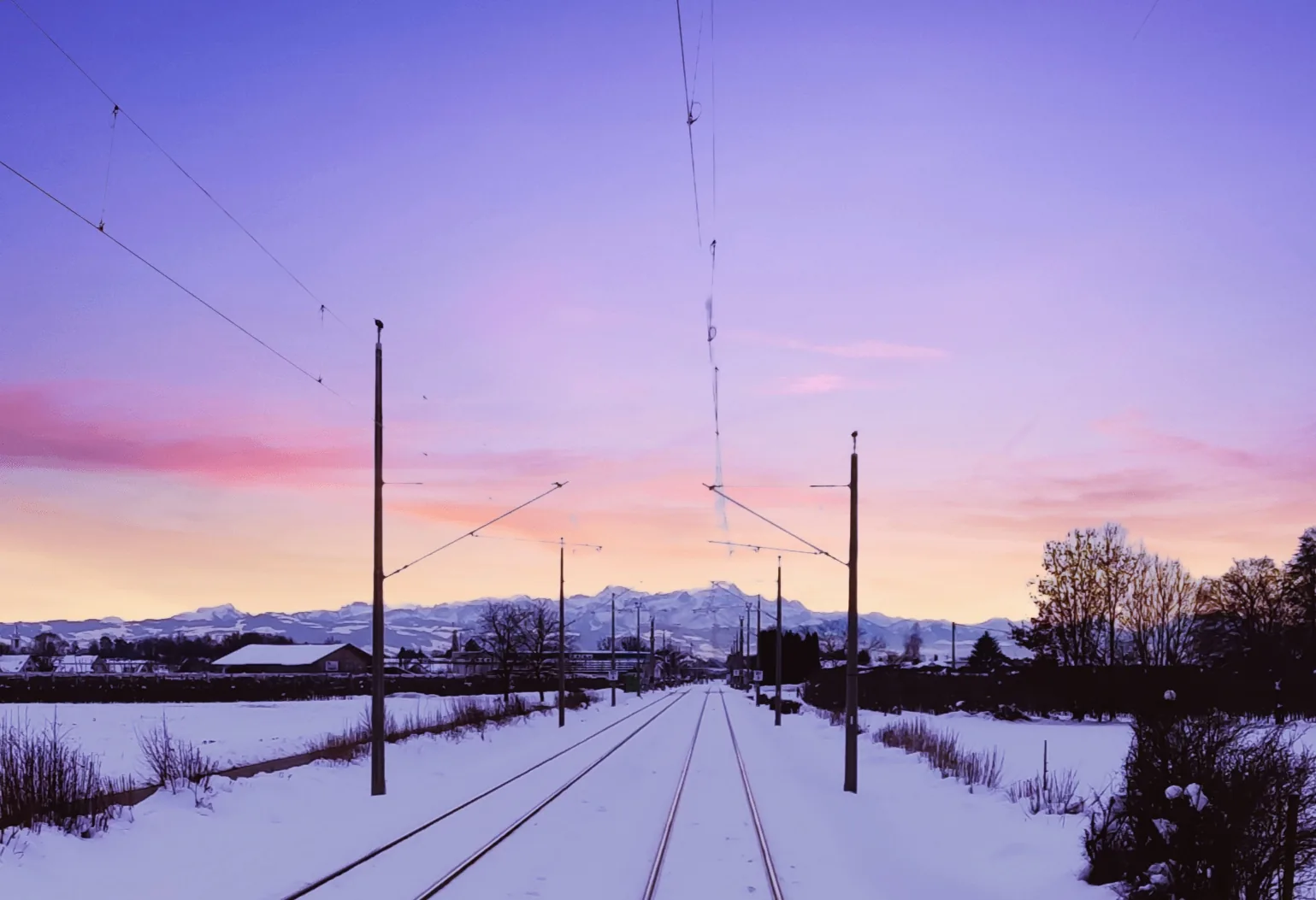Verschneite Bahnstrecke vor den Alpen